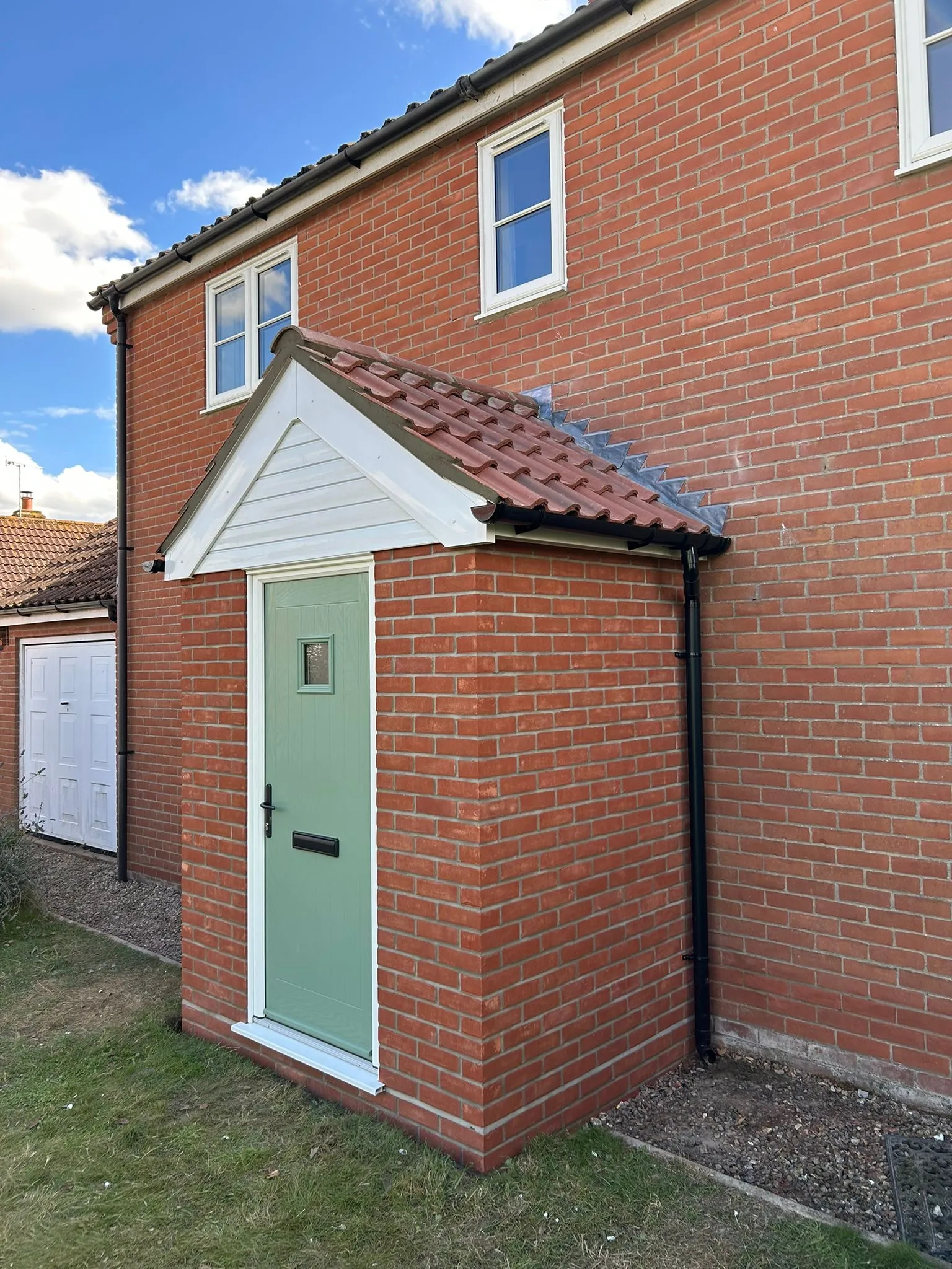 A newly built enclosed brick porch with a sage green composite front door and tiled pitched roof on a red brick home in Norwich