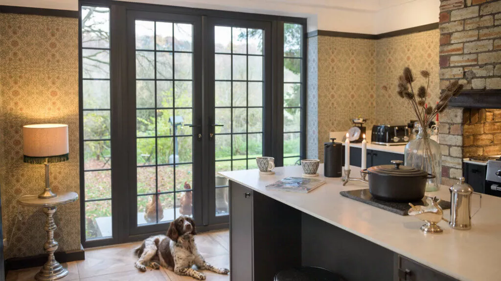 Grey French doors with glazing bars opening from a cottage kitchen onto the garden