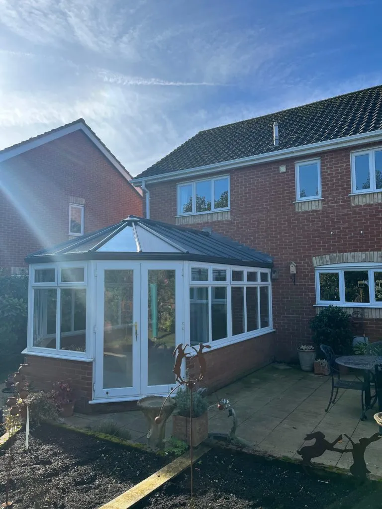 Victorian-style conservatory with a glass roof and white French doors on a red-brick home in Dereham