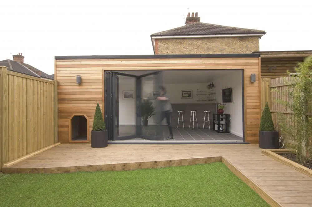 Anthracite bi-fold doors opening a timber-clad garage conversion onto a decked garden in Drayton