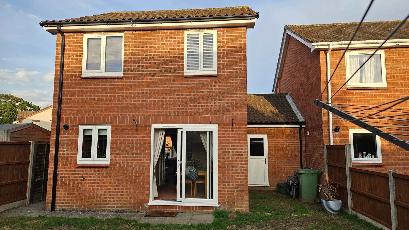 Rear of a brick house in Drayton NR8 after replacement, with white uPVC windows, a white uPVC sliding patio door, a white back door and new fascias and guttering