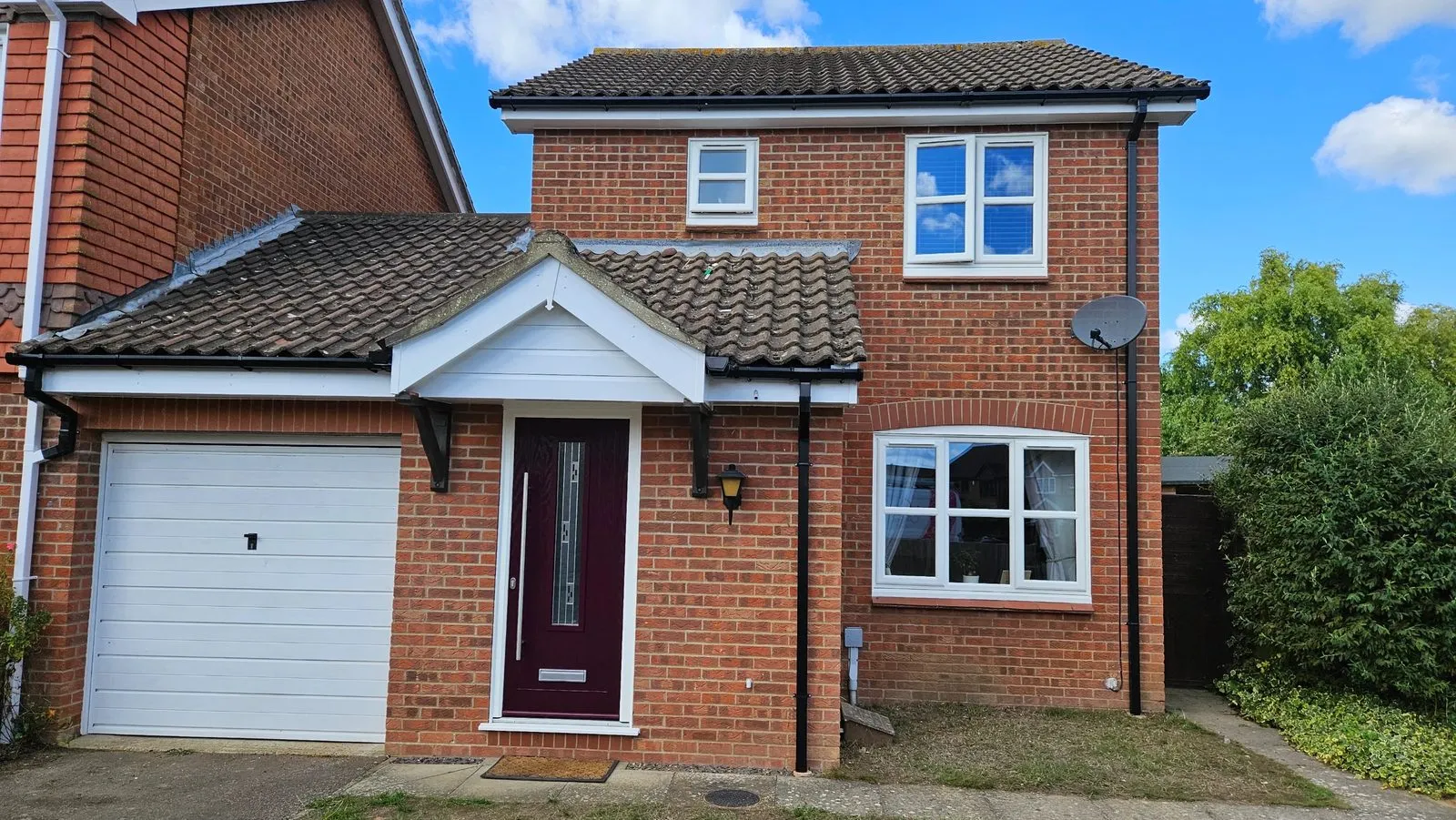 Brick house in Drayton NR8 after replacement, with white uPVC casement windows, a deep red composite front door, a white clad porch gable and new fascias and black guttering
