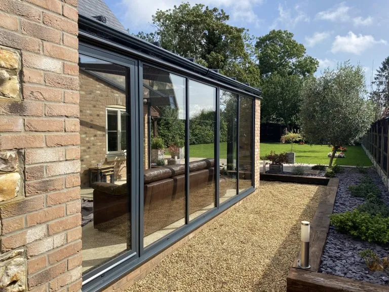 Anthracite grey aluminium lean-to conservatory with a glass roof beside a garden path in Crimplesham