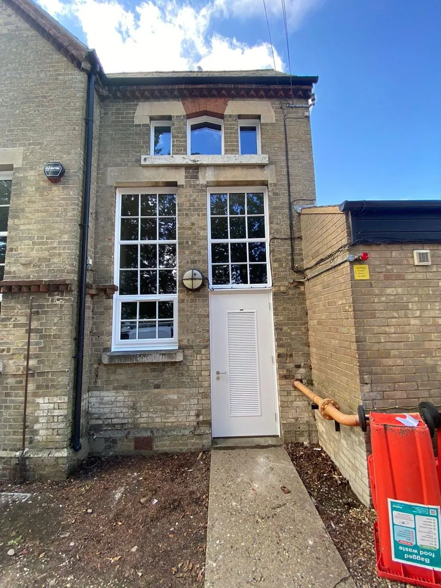 White steel louvred boiler room door with new white uPVC windows and high-level windows above at Horsford CofE VA Primary School