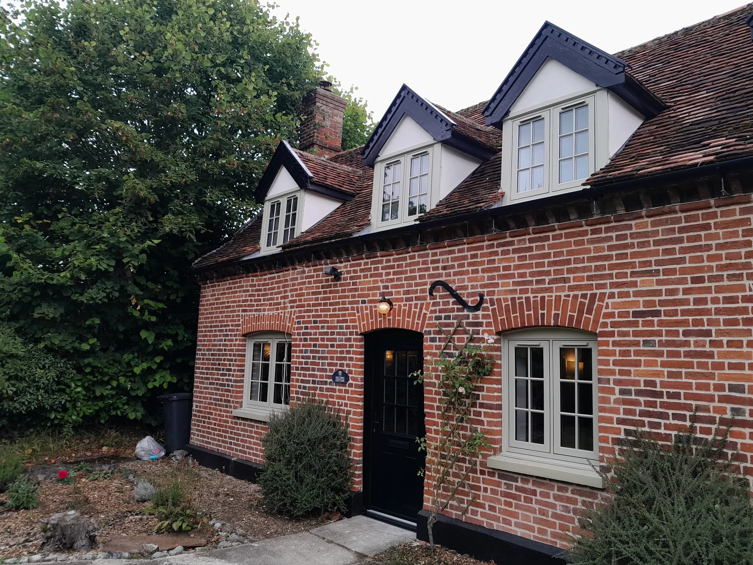 Olive grey timber-look PVC flush casement windows with Georgian bars and black composite front door at Old Rectory Cottage, Langham IP31 — wider front elevation