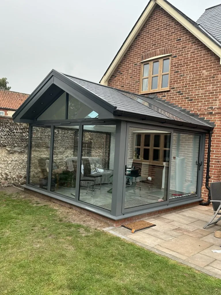 Anthracite grey conservatory with a tiled-effect roof and glazed gable on a red-brick period home in NR13