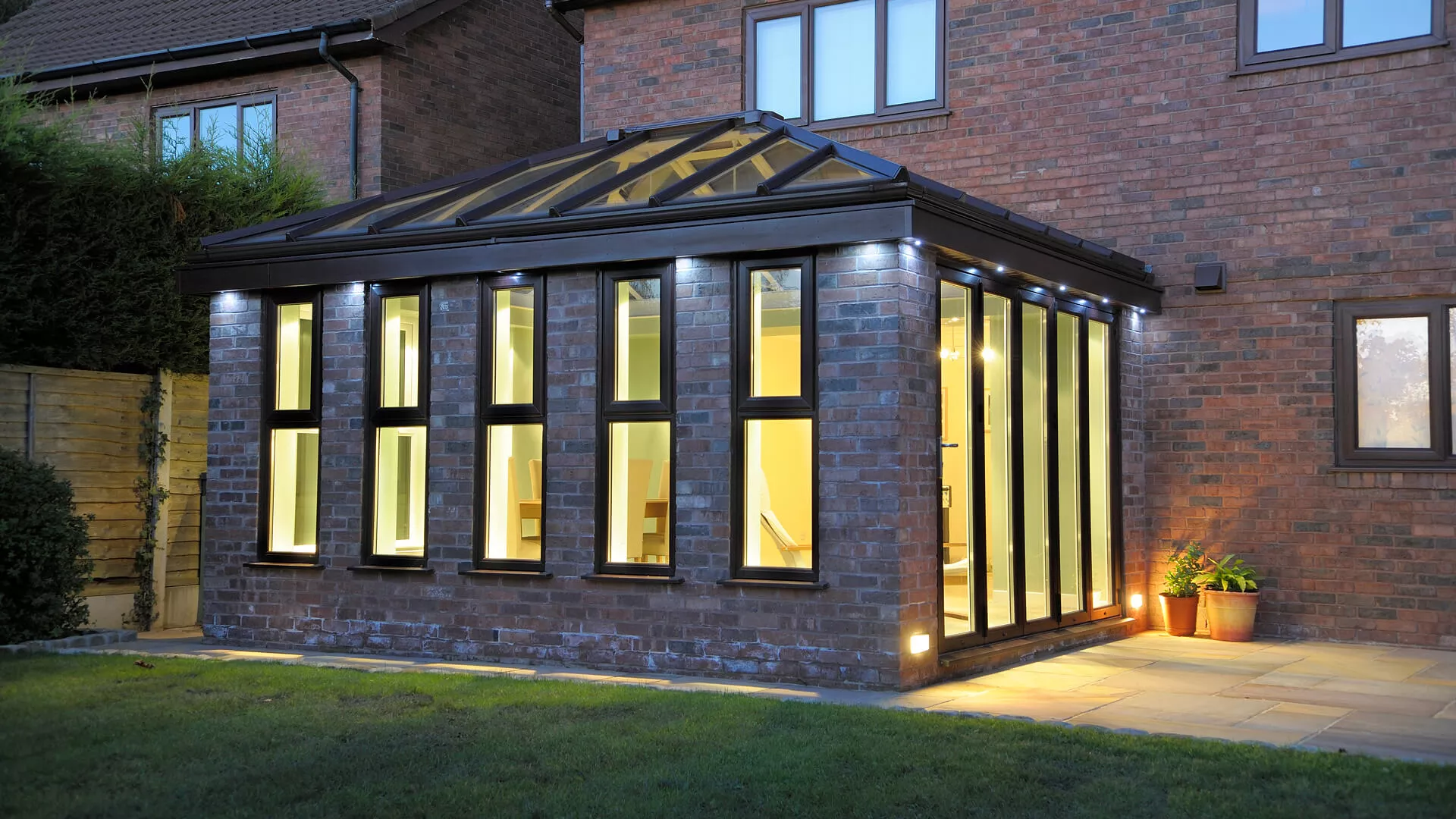 Contemporary orangery with dark grey frames, a roof lantern and lit interior at dusk