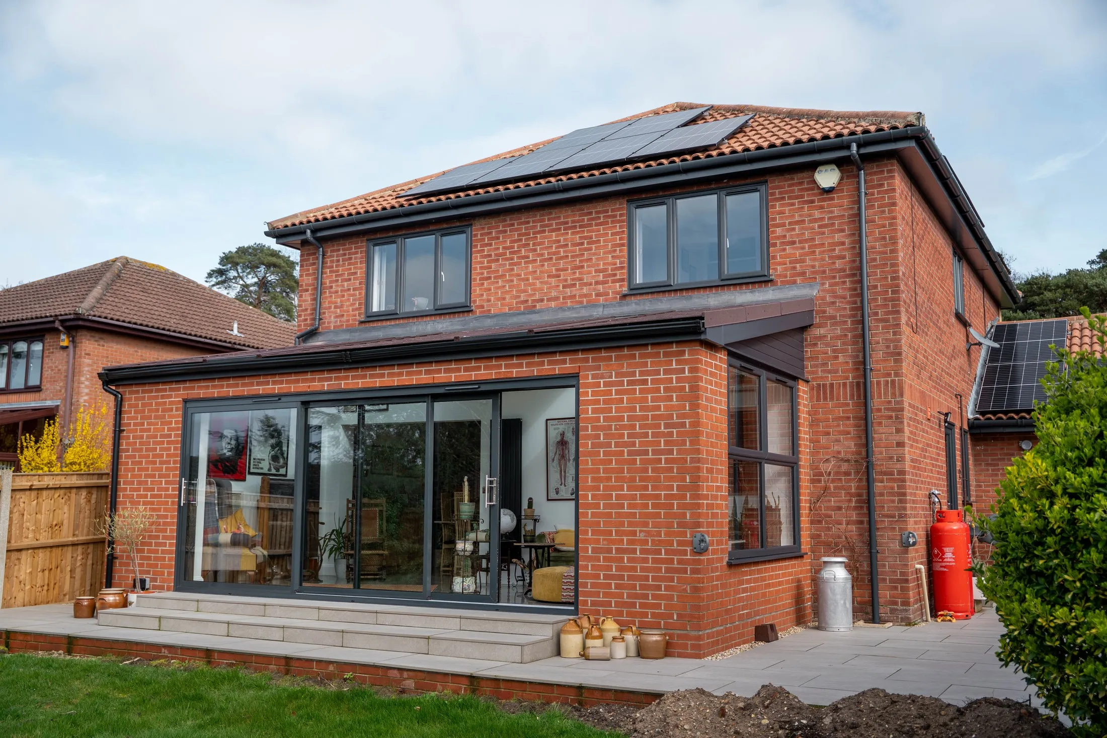 Brick rear extension with anthracite sliding doors and grey patio, St Olaves NR31, replacing a glass conservatory