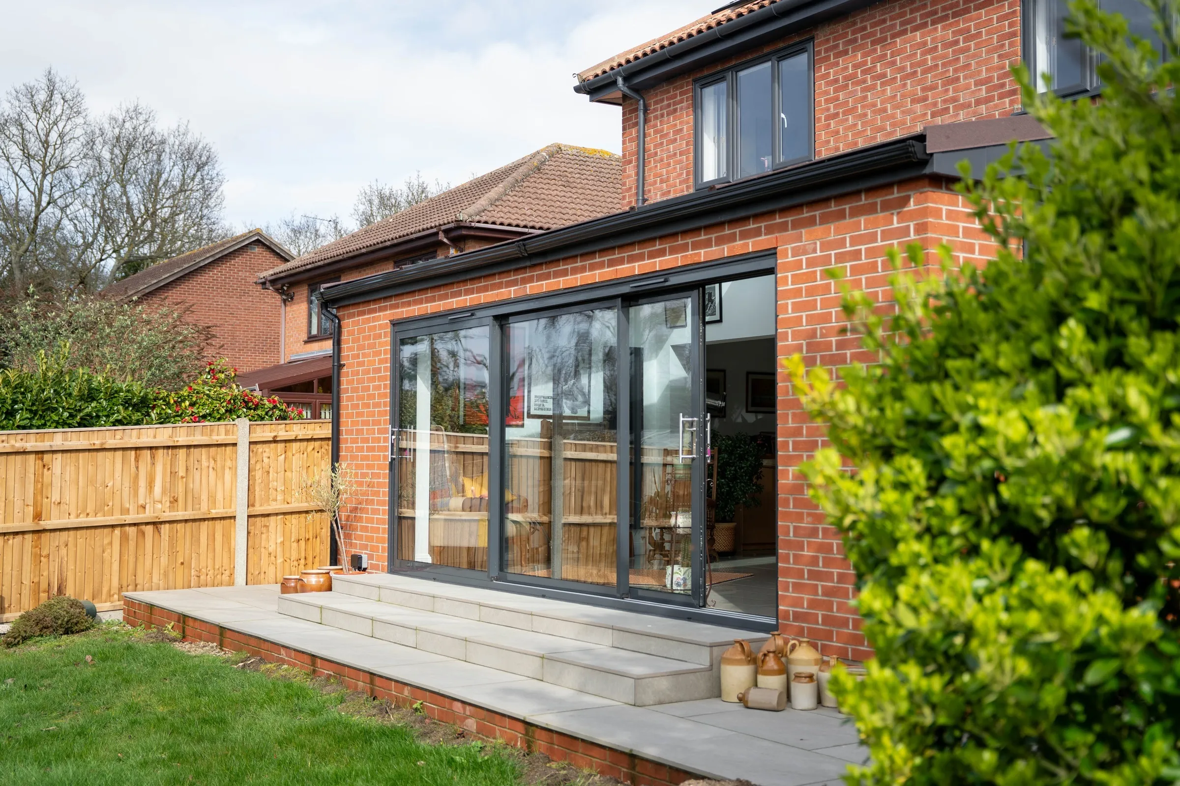 Brick rear extension with anthracite aluminium triple-track sliding doors onto a new patio, St Olaves NR31