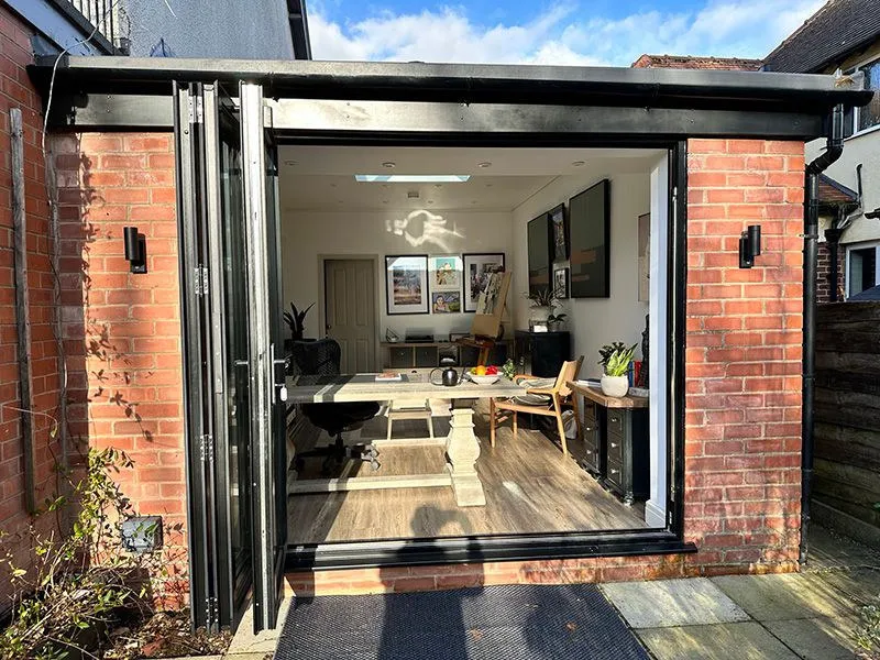 Brick garage conversion home office with open black bifold doors onto a patio, Wymondham area